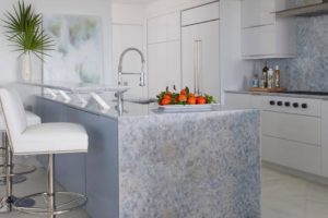 Modern kitchen with grey island, tall white chairs at the island, built-in appliances, and cabinets in sleek white.