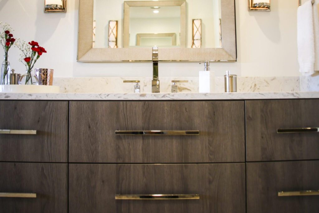 Close-up of bathroom vanity in medium dark wood grain and marble countertop with gold drawer handles