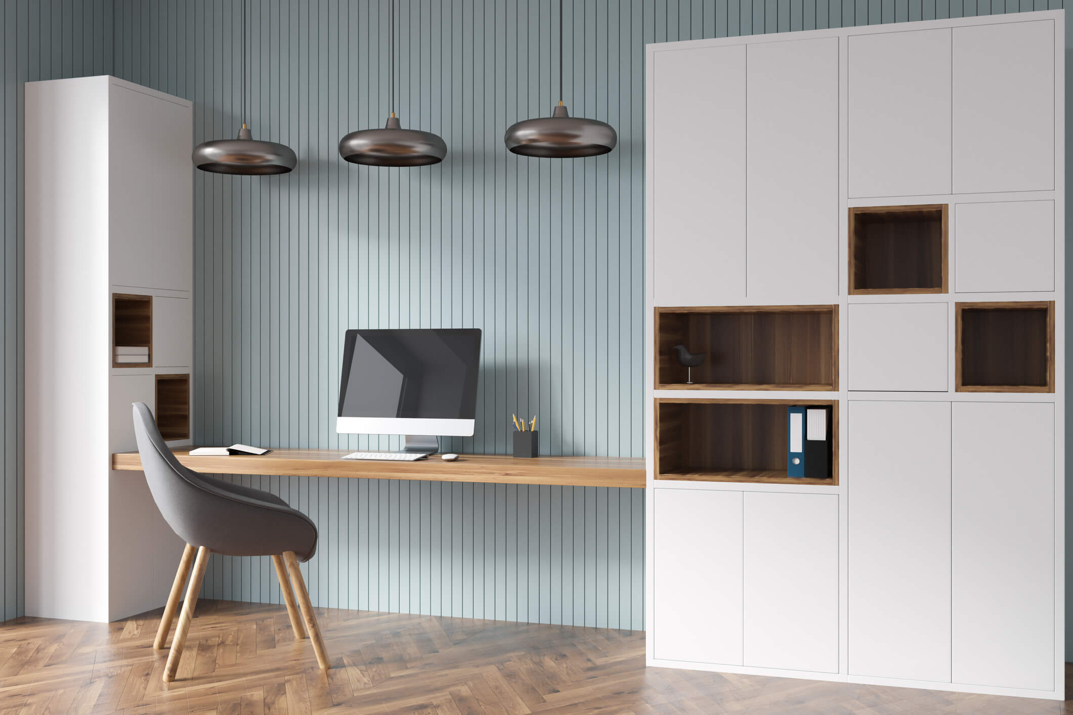 Modern open office with custom cabinets, open shelving, and a chair facing a floating wooden desk with a Mac on it. 3 hanging lighting are over the desk.