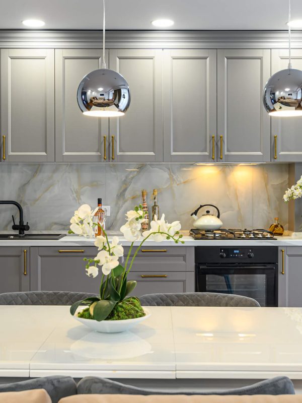 Contemporary kitchen with grey Shaker cabinets, a white table with grey chairs and flowers on the table, and 2 silver hanging lights.