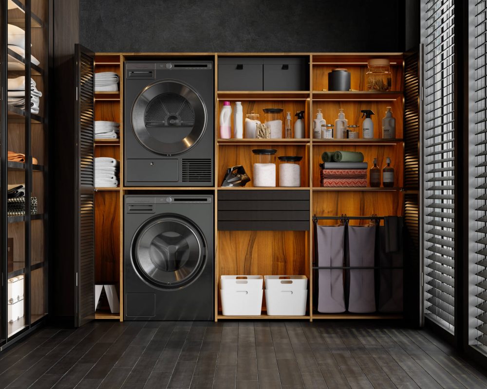 Modern laundry room with a stacked, black washer and dryer and open shelving with laundry supplies. Slat blinds on the windows and wood flooring.