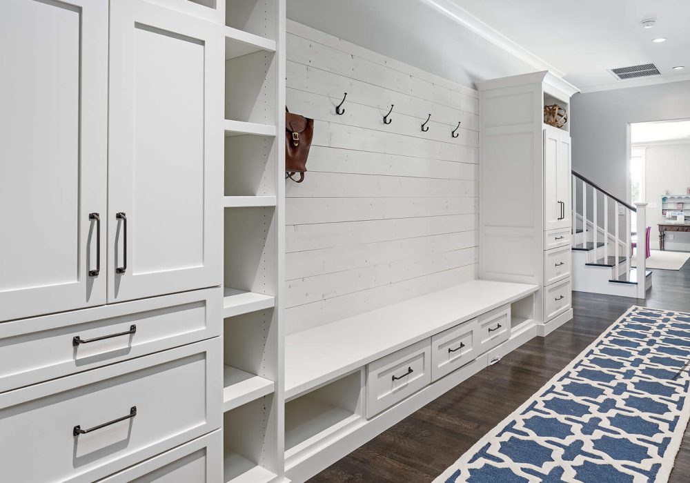 Mudroom/hallway/entryway with white built-in cabinets, low storage drawers, and a bench. All in white wood. There is a long blue and white runner on the dark wood floor.